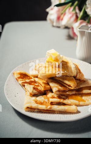 Deliziosa colazione con frittelle dorate ricoperte di burro fuso e miele sgocciolato. Perfetto per un'accogliente sorpresa mattutina, che porta calore e calore Foto Stock