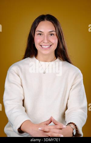 Giovane donna che sorride, indossa un maglione e gioielli, incrocia le mani Foto Stock
