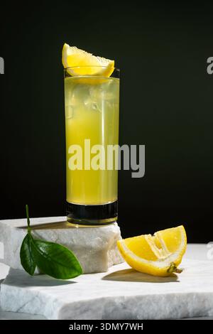Un rinfrescante bicchiere di tè al limone si trova elegantemente su una superficie di marmo bianco. La guarnizione a spicchi di limone aggiunge un tocco vivace a questo fresco e dissetante Foto Stock
