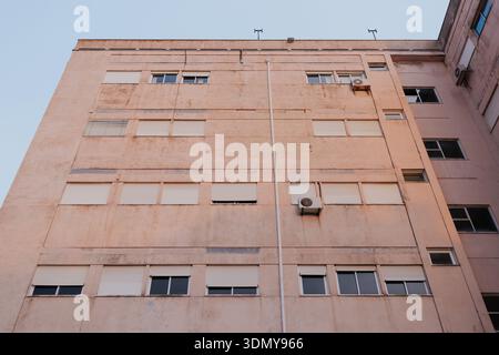 Una grande facciata residenziale con finestre chiuse che mostrano unità di aria condizionata e pareti usurate. L'immagine acquisisce la trama e il colore del Foto Stock