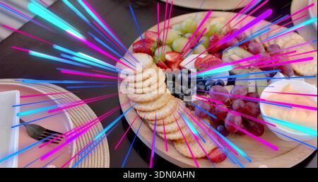 Piatto di legno con cracker, uva, fragole, formaggio, immersione su tavola scura, striature al neon Foto Stock