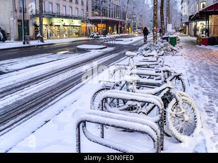 Parigi, Francia. La scena stradale invernale presenta biciclette innevate parcheggiate sul marciapiede lungo Avenue de Clichy durante una giornata fredda Foto Stock