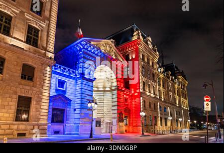L'edificio della Prefettura della polizia sull'Ile de la Cité presenta una bandiera francese tricolore blu, bianca e rossa sull'ingresso dell'arco in pietra di notte a Parigi, Francia Foto Stock