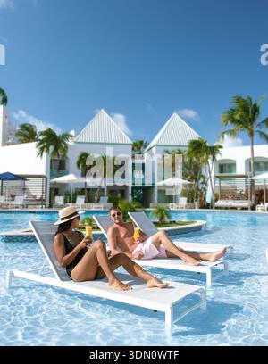 Due amici si rilassano vicino alla piscina in uno splendido resort di Aruba, gustando un drink tropicale sotto il sole luminoso. Le palme oscillano delicatamente, creando una scena perfetta Foto Stock