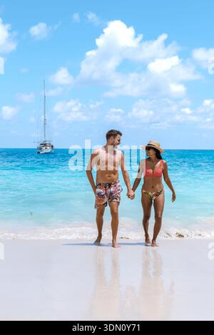 Un paio cammina mano nella mano lungo la tranquilla spiaggia di Anse Georgette, Praslin Seychelles, godendosi il caldo sole e le acque cristalline. Foto Stock