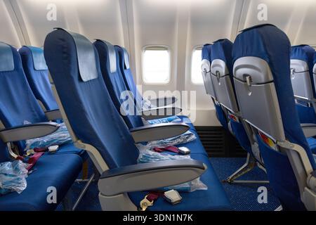 Fila di sedili blu all'interno di un moderno aereo commerciale con finestre luminose, braccioli e cinture di sicurezza visibili. Cabina economica pulita e vuota per i viaggi e l'aviazione Foto Stock