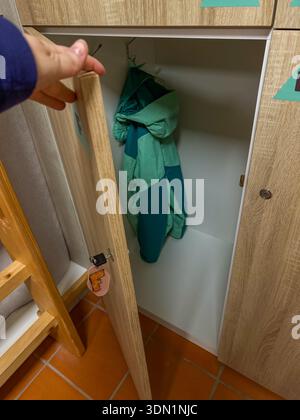 Armadietto aperto dell'ostello con porta in legno, giacca appesa all'interno, spazio di stoccaggio compatto nel dormitorio condiviso. Sistemazione economica, viaggi per backpacker Foto Stock