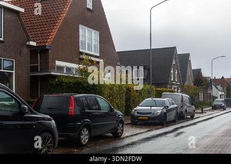 Tranquille case in mattoni del villaggio olandese di Hattem, tetti inclinati, auto parcheggiate e asfalto bagnato sotto il cielo coperto. Architettura tradizionale, autunno Foto Stock