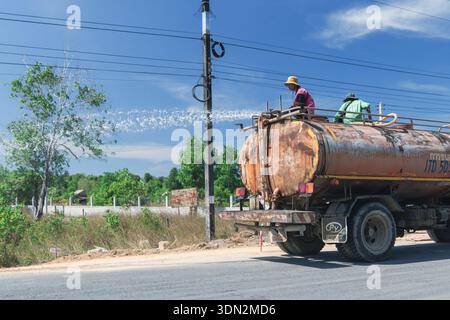 Koh Kho Khao Island Tailandia 04 01 2026: Manutenzione stradale industriale - Rusty Tanker Truck con lavoratori che innaffiano e irrigano polvere di controllo stradale Foto Stock
