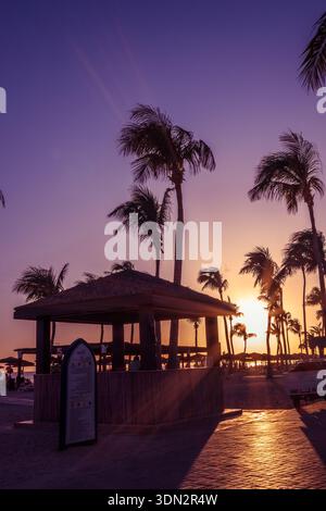 Una splendida scena al tramonto sulla spiaggia di Salalah dell'Oman Hawana, caratterizzata da palme sagomate e un affascinante bar tiki. Il cielo vanta vibranti porpora e orano Foto Stock