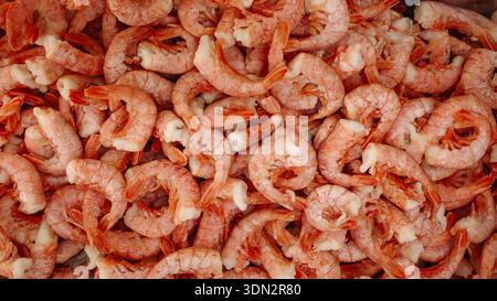 Gamberetti surgelati e non sbucciati con fondo di pesce. Cumulo di gamberetti crudi non pelati congelati con conchiglie, fondo di consistenza di pesce per esposizione sul mercato, imballaggio Foto Stock