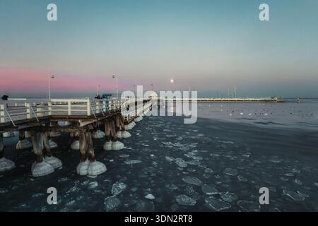 Un'affascinante e ampia ripresa orizzontale del molo di Sopot che si estende nel Mar Baltico parzialmente congelato al crepuscolo in Polonia. Il molo di legno, adornato con W Foto Stock
