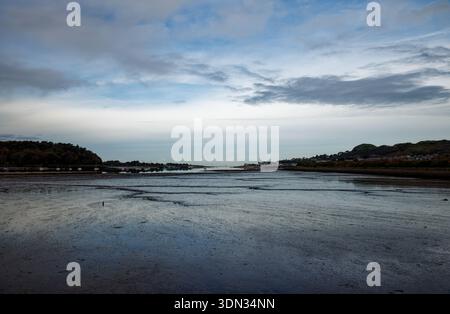 La luce acquosa si riflette sulle piane umide di fango di un estuario durante la bassa marea con colline su entrambe le sponde e il mare in lontananza, Conway, Galles del Nord. Foto Stock