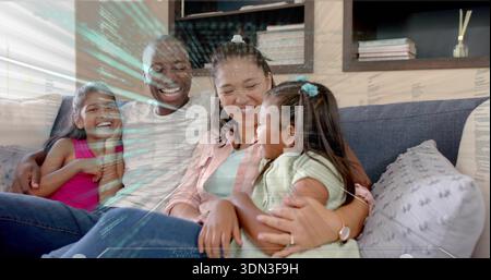 Famiglia sorridente di quattro persone che si accoccolano sul divano grigio nel soggiorno, indossano camicia rosa e rivestimento in HUD Foto Stock