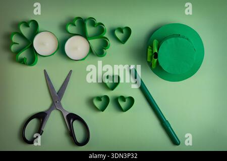Gli utensili fai-da-te con forature in shamrock verde e un cappello da leprechaun sono disposti su uno sfondo verde chiaro in una composizione con vista dall'alto e spazio per le copie. Foto Stock