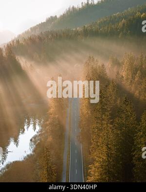 Vista aerea di una strada che attraversa una foresta nebbiosa, bagnata dal caldo bagliore dei raggi del sole, Garmisch-Partenkirchen, Baviera, Germania. Foto Stock