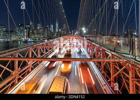 La vista notturna delle luci sfocate delle auto attraversa il Ponte di Brooklyn, giustapposta allo scintillante paesaggio urbano di Manhattan, New York, Stati Uniti. Foto Stock
