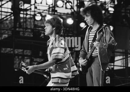Questa fotografia in bianco e nero del 1982 cattura Mick Jagger e Bill Wyman dei Rolling Stones che si esibiscono dal vivo sul palco. Jagger, indossando una camicia a motivi geometrici, tiene in mano una chitarra, mentre Wyman, con una camicia e una giacca a righe, suona il suo basso, entrambi impegnati in un dinamico ambiente da concerto. Foto Stock