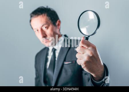 Uomo d'affari che ispeziona attentamente i documenti finanziari con lente d'ingrandimento, concetto di audit delle entrate, attenzione selettiva Foto Stock