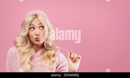 Giovane donna che masticava Gum e faceva un'espressione giocosa su uno sfondo rosa Foto Stock