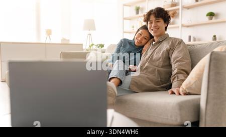 Giovani coppie sedute insieme sul divano e godersi il tempo guardando uno schermo in una stanza accogliente Foto Stock