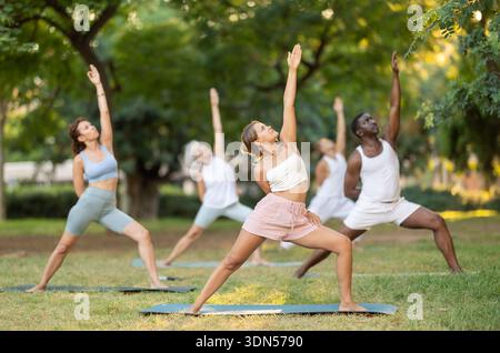 Persone di età e nazionalità diverse praticano varie pose yoga nel giardino estivo Foto Stock