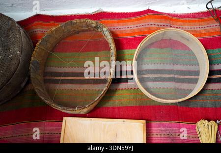 Setacciatori tradizionali in legno e setacci di farina su un vibrante tappeto greco intrecciato a mano. Autentica cucina rustica. Foto Stock