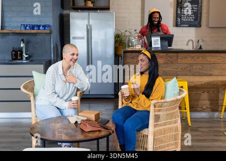 Diverse amiche che parlano al caffè intorno a un tavolo di legno con scatola di pasticceria e tazze da caffè da asporto Foto Stock