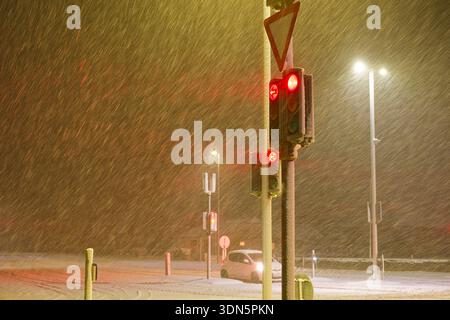 I semafori rossi brillano attraverso forti nevicate in una notte d'inverno nel nord Europa, simboleggiando la sicurezza stradale la bassa visibilità il rischio di mobilità urbana e.. Foto Stock