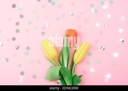 Tulipani rossi e gialli su sfondo rosa con coriandoli. Concetto di vacanze primaverili. Vista dall'alto, disposizione piatta. Foto Stock