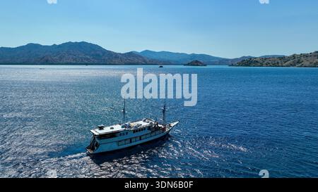 Una tradizionale barca indonesiana in legno phinisi galleggia pacificamente sulle acque calme e blu del mare sotto un cielo luminoso e soleggiato. Foto Stock