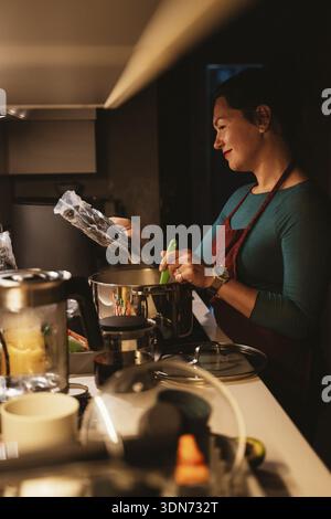 Donna sorridente mentre usa la tecnica sous vide in cucina. Prepara il cibo con attenzione e piacere, mostrando metodi culinari moderni. Lo scen Foto Stock