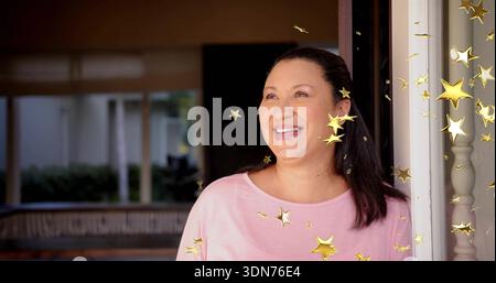 Donna matura sorridente in piedi sulla porta vicino alla ringhiera del portico in cima rosa, con sovrapposizioni a stelle dorate Foto Stock