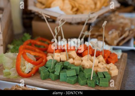 Un vivace tagliere di salumi presenta formaggi assortiti, peperoni rossi freschi, cubetti di erbe verdi e lattuga croccante, ideale per feste o catering Foto Stock