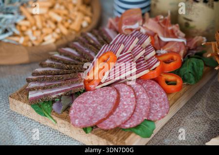 Un tagliere di salumi ben organizzato con salumi, salumi, prosciutto, peperoni rossi, spinaci, e grissini su un piatto di legno rustico, Foto Stock