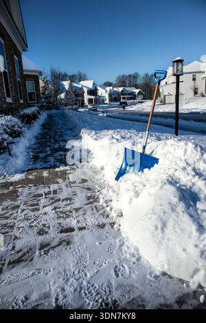 Marciapiede di periferia con pala da neve blu dopo una nevicata fresca Foto Stock