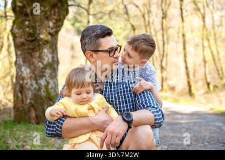 Padre che abbraccia con bambini all'aperto nella foresta. Foto Stock