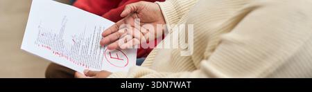 Intestazione della donna nera di mezza età che tiene in mano la carta di prova non superata con grande rosso grado F, gesti con la mano mentre discute il risultato, vista parziale del bambino sullo sfondo Foto Stock