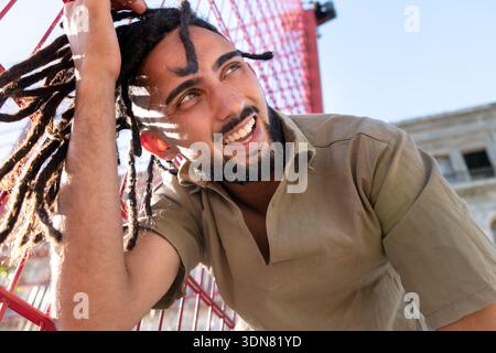 Uomo con dreadlock che sorride brillantemente, si sente felice nel caldo sole estivo Foto Stock