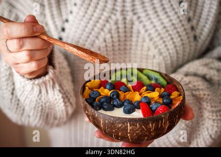 Donna che mangia una sana colazione dalla ciotola di cocco. Yogurt con fiocchi di mais e frutti di bosco Foto Stock