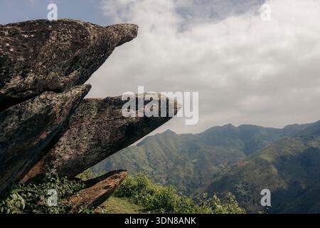 Affioramento roccioso che si affaccia su lussureggianti montagne verdi sotto un cielo parzialmente nuvoloso. Montagne di Ta Xua, distretto di Bac Yen, Son la, Vietnam Foto Stock