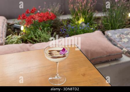 panna cotta alla vaniglia setosa e cremosa servita in un elegante calice di vetro, splendidamente condita con un ricco goccio di cioccolato e un delicato fl commestibile viola Foto Stock