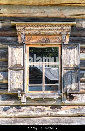 Finestra di un'antica casa in legno tradizionale russa con finiture in legno intagliato e persiane Foto Stock