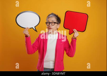 Una donna anziana con occhiali eleganti e capelli grigi tiene una bolla bianca in una mano e una bolla rossa nell'altra, sottolineando la comunita' Foto Stock