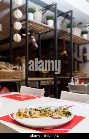 tagliatelle cremose condite con teneri pezzi di pollo alla griglia e guarnite con erbe fresche, perfettamente abbinate a un fresco bicchiere di bianco vincente Foto Stock