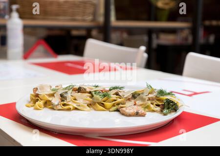 tagliatelle cremose condite con teneri pezzi di pollo alla griglia e guarnite con erbe fresche, perfettamente abbinate a un fresco bicchiere di bianco vincente Foto Stock