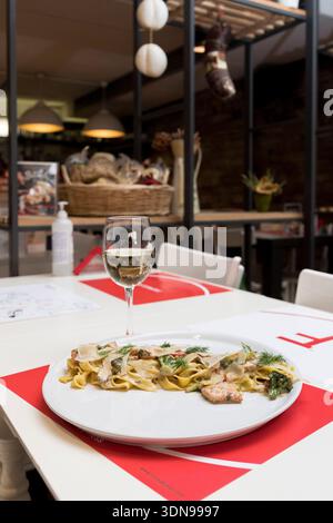tagliatelle cremose condite con teneri pezzi di pollo alla griglia e guarnite con erbe fresche, perfettamente abbinate a un fresco bicchiere di bianco vincente Foto Stock