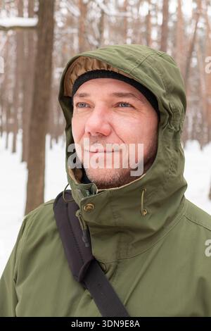 Occhi azzurri. Ritratto maschile. Vestiti invernali. Giacca con cappuccio. Uomo di oltre 40 anni sorridente. Mezza età. Stile di vita attivo. Clima invernale. Camminare in inverno Foto Stock