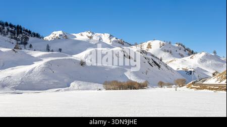 Un panoramico panorama invernale di neve profonda che copre le pendici del Colle della Maddalena sotto un cielo azzurro e luminoso. Foto Stock