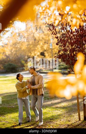 Sotto le foglie d'autunno dorate, una donna coreana e un uomo caucasico condividono una danza gioiosa nel parco, abbracciando la bellezza della stagione. Foto Stock